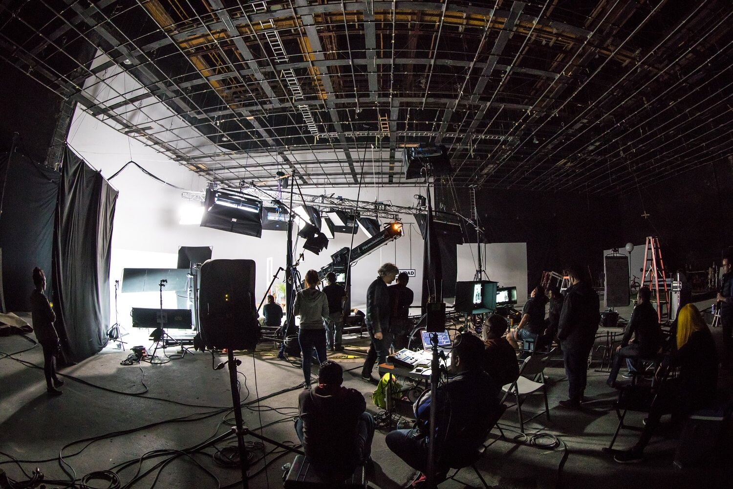 Verschiedene Personen aus einer Filmcrew arbeiten an Filmset, an dem bereits verschiedene Kameras und Lichtboxen aufgebaut wurden.