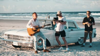 Ein Sänger mit einer Gitarre sitzt in einem Musikvideo, das ebenfalls zu den Kurzfilmen zählt, auf einer Autohaube.