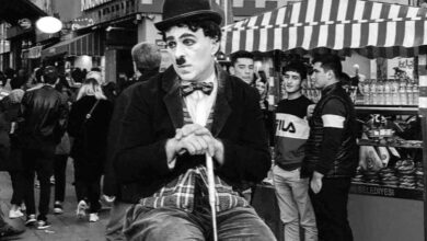 Mann verkleidet als Stummfilmkomiker Charlie Chaplin sitzt auf einem Stuhl.