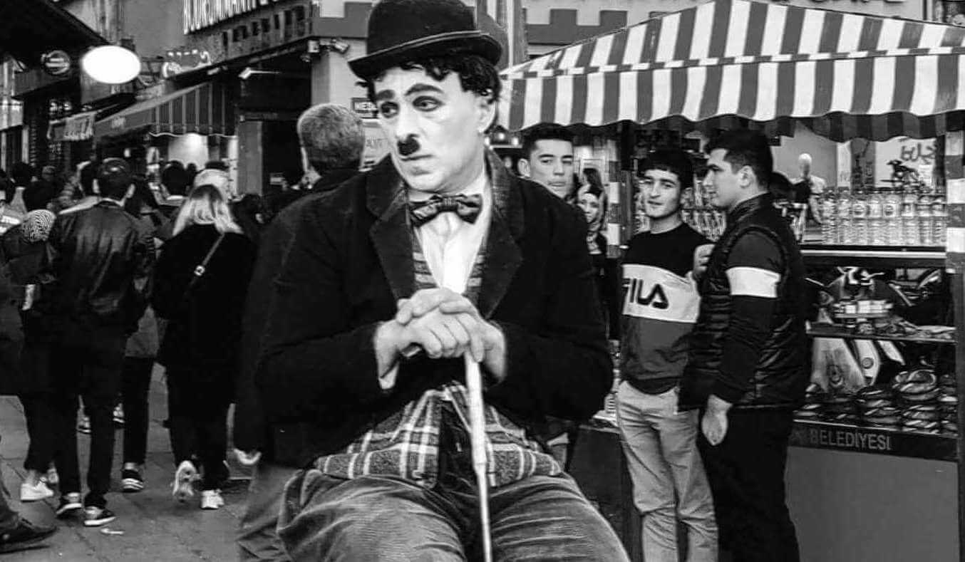 Mann verkleidet als Stummfilmkomiker Charlie Chaplin sitzt auf einem Stuhl.