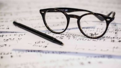 Eine schwarze Brille und Stift auf einem Blattpapier mit Musiknoten, erstellt von einem Filmkomponist, drauf