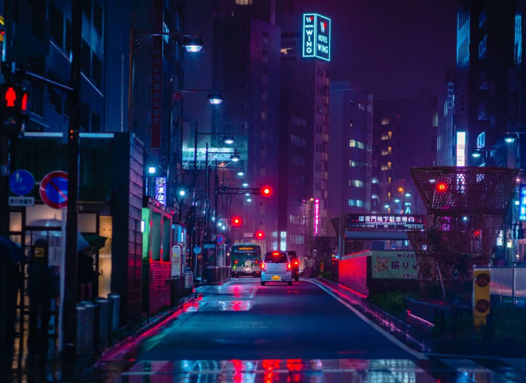 Auf dem Bild ist eine verregnete Straße zu sehen, die mit Neonschildern beleuchtet wird.